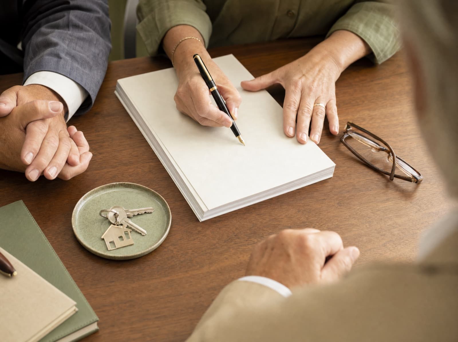 Closing documents, a pen mid signature, and a set of keys on a conference table